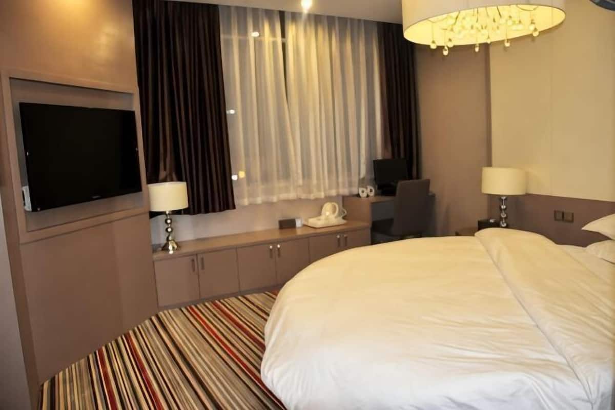 Ein Hotelzimmer mit einem großen Bett, einem wandmontierten Flachbildfernseher, einem Schreibtisch mit Lampe und einem fenster mit Vorhängen.