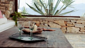 Una mesa de madera rústica con dos vasos transparentes y una vela, frente a una pared de piedra con vistas a una montaña y plantas.
