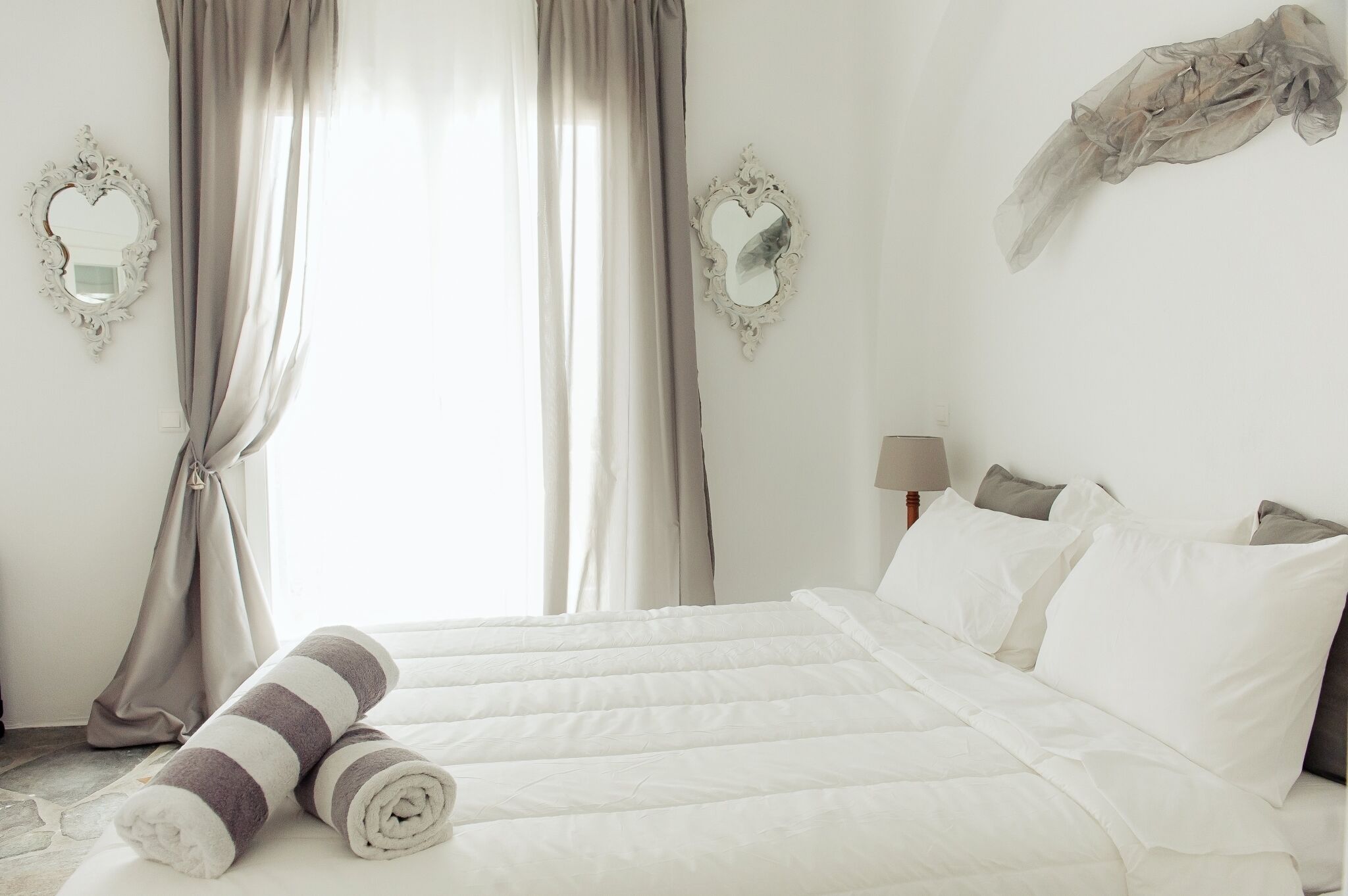 A neatly made bed with white and gray striped towels, a lamp, and two heart-shaped mirrors on the walls.