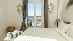 Un dormitorio con una cama grande, dos espejos laterales, vista al mar y una cesta de mimbre en el suelo.
