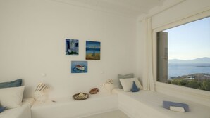 Habitación minimalista con un ventanal grande con vistas a la costa, que incluye un sofá blanco, una mesita y tres cuadros en la pared.