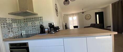 A modern kitchen with a central island, built-in oven, coffee maker, and hanging pendant lights.