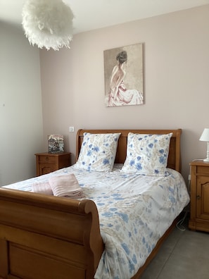 Un dormitorio con cama de madera, ropa de cama floral, una mesita de noche con lámpara y un cuadro en la pared.