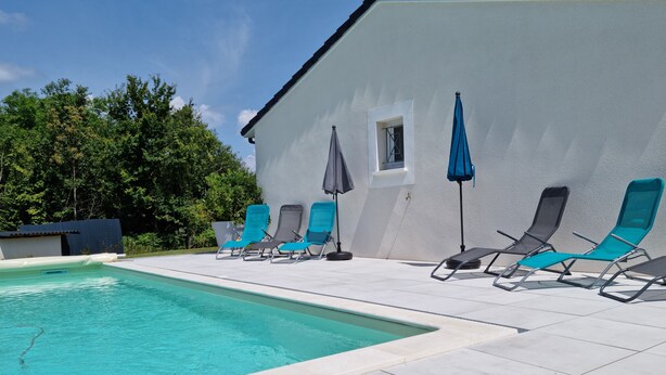 A swimming pool with lounge chairs and umbrellas, surrounded by a white building and trees.