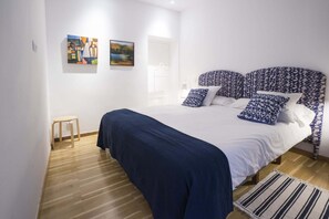 A bedroom with a bed, a small stool, and two artworks on the wall.