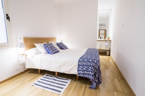 A bedroom with a bed, bedside lamps, a bedside table, a window, a mirror, and a wooden floor.