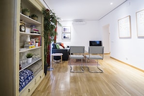 A modern living room with a sofa, two chairs, a TV, and a bookshelf with decorative items.