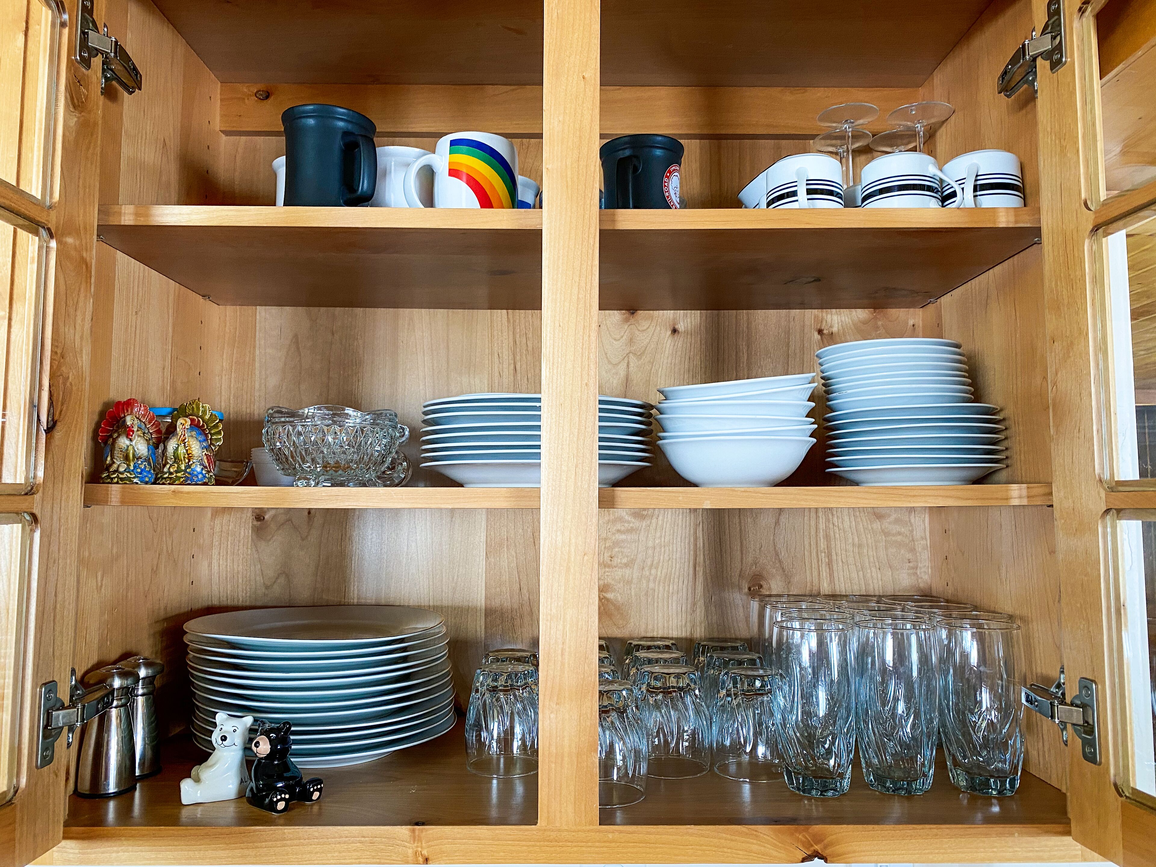 A wooden cabinet with shelves containing various kitchenware, including plates, bowls, and glassware.
