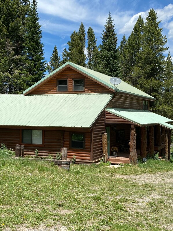 Eine Blockhütte mit grünem Metall-Dach, einer Veranda und einer sichtbaren Satellitenschüssel.