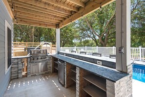 Enjoy outdoor dining and cooking under a shaded pergola with a gas grill and refrigerator.
