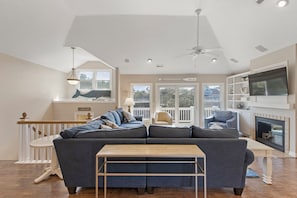 A living room with a sectional sofa, a wooden coffee table, a fireplace, and a television mounted on the wall.