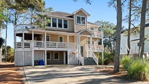 A two-story house with a balcony on the upper floor, a covered porch on the lower floor, and a driveway leading to the entrance. - Endless Sunsets in Corolla Light: Pool, Spa, Club Amenities & Golf Discounts! (Corolla)