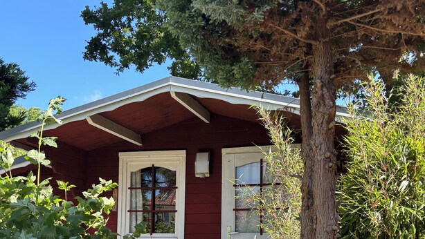 A red wooden house with a white porch and a white chair.