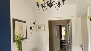 A hallway with a wooden table, a vase with green plants, a framed picture, and a chandelier.