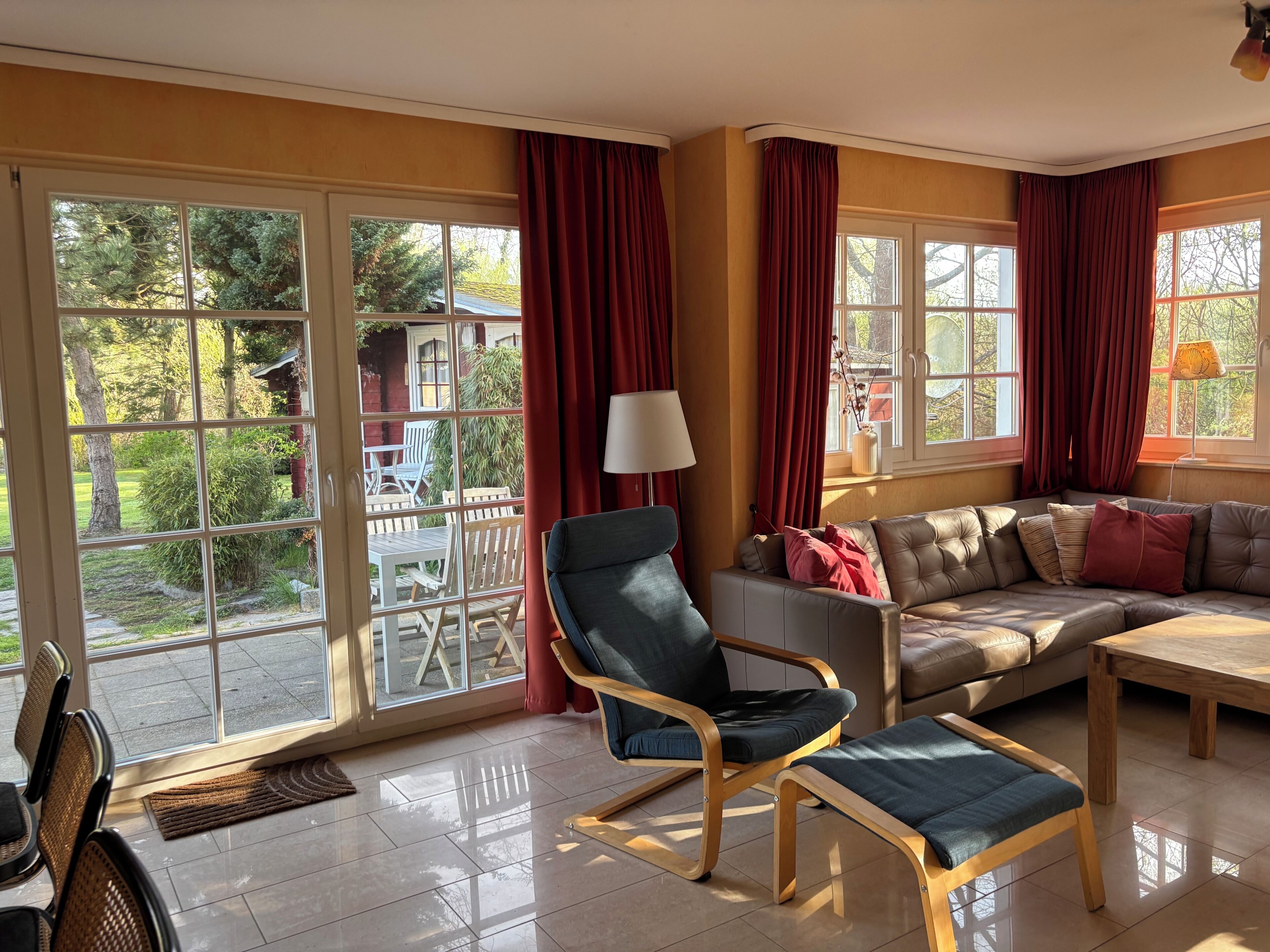 Ein geräumiges Wohnzimmer mit einer großen Glasschiebetür, die auf eine Terrasse im Freien führt, einem Ledersofa, einem Holztisch und einem modernen Sessel.