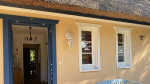 A building entrance with a blue door, a bench outside, and a thatched roof.
