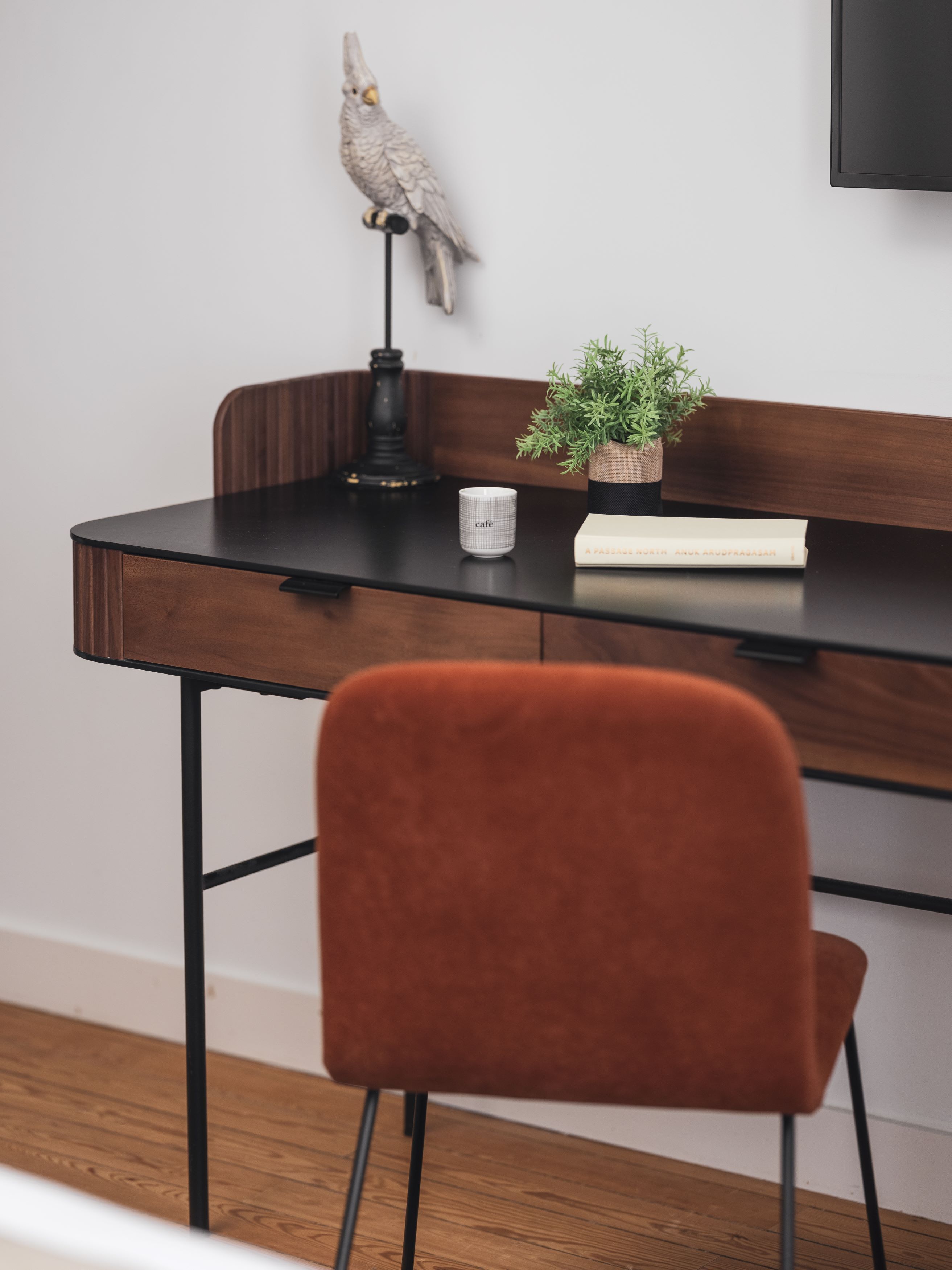 Un bureau moderne avec une chaise marron, une petite plante en pot, une lampe et une tasse.
