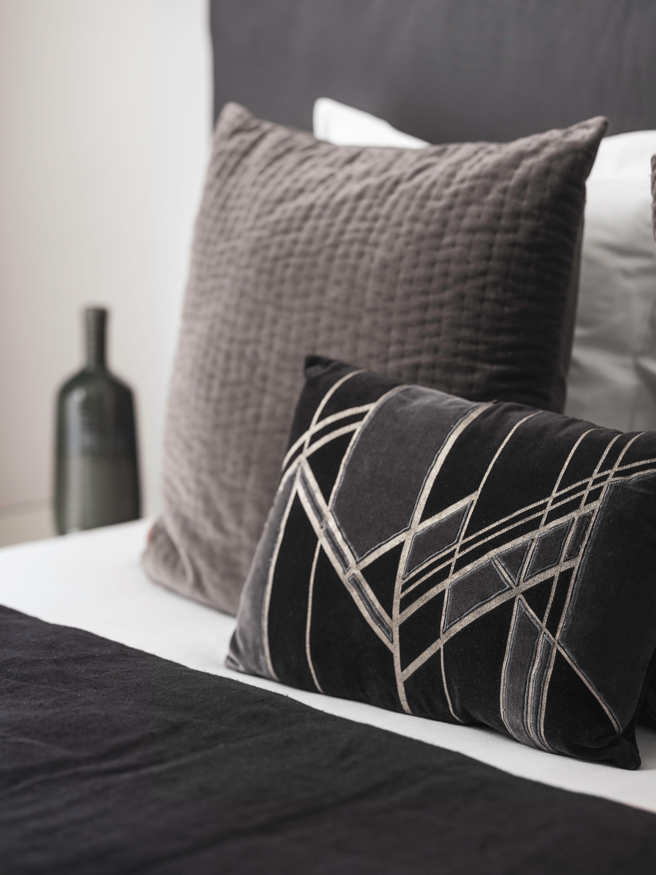 Una cama con un cojín estampado en blanco y negro y un cojín gris con textura.