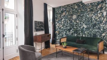 A modern living room with a green sofa, a grey armchair, a wooden coffee table, and a TV mounted on the wall.