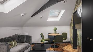 A modern loft apartment with a high ceiling, skylights, a cozy seating area with a sofa and chairs, a small round table, and a fireplace.