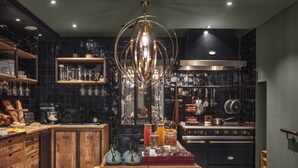 A modern kitchen with a wooden table, black tiled backsplash, and stainless steel appliances. - Appartements Crébillon - Maisons du Monde Hôtel & Suites (Nantes)