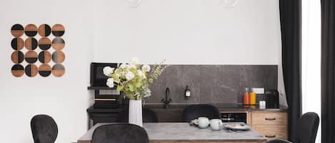A modern kitchen with a wooden table, black chairs, a vase with flowers, and a hanging light fixture.
