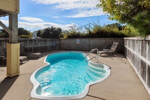 Une piscine avec une terrasse en bois, des chaises longues et une clôture en bois.