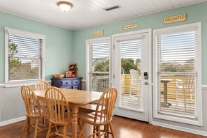 A dining area with a wooden table and chairs, white-framed doors with blinds, and a sign that reads "DELIGHTED". - A Shore Thing In Duck: Oceanside, Private Pool (Duck)