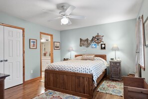 A bedroom with a wooden bed, a ceiling fan, a wall clock, and a small cabinet. - Teacher's Lair: Oceanview, Short Walk to Beach (Nags Head)
