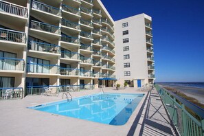 A multi-story hotel with balconies, a swimming pool, and a view of the beach.
