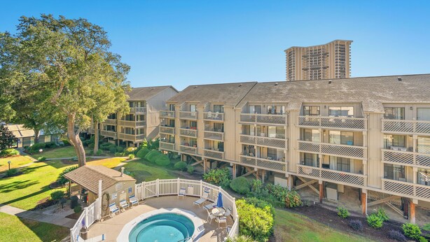 A multi-story hotel with a pool area, outdoor seating, and a tall building in the background.