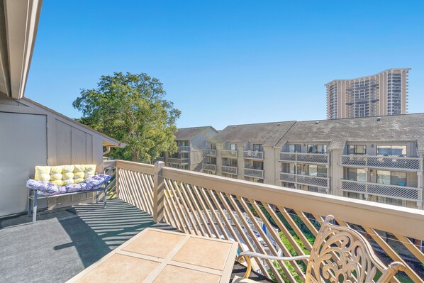 Un balcon avec un banc rembourré, une petite table et une balustrade.