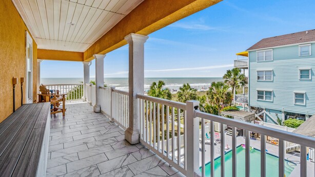 A covered balcony with a view of the beach and a pool area.