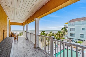 A covered balcony with a view of the beach and a pool area.