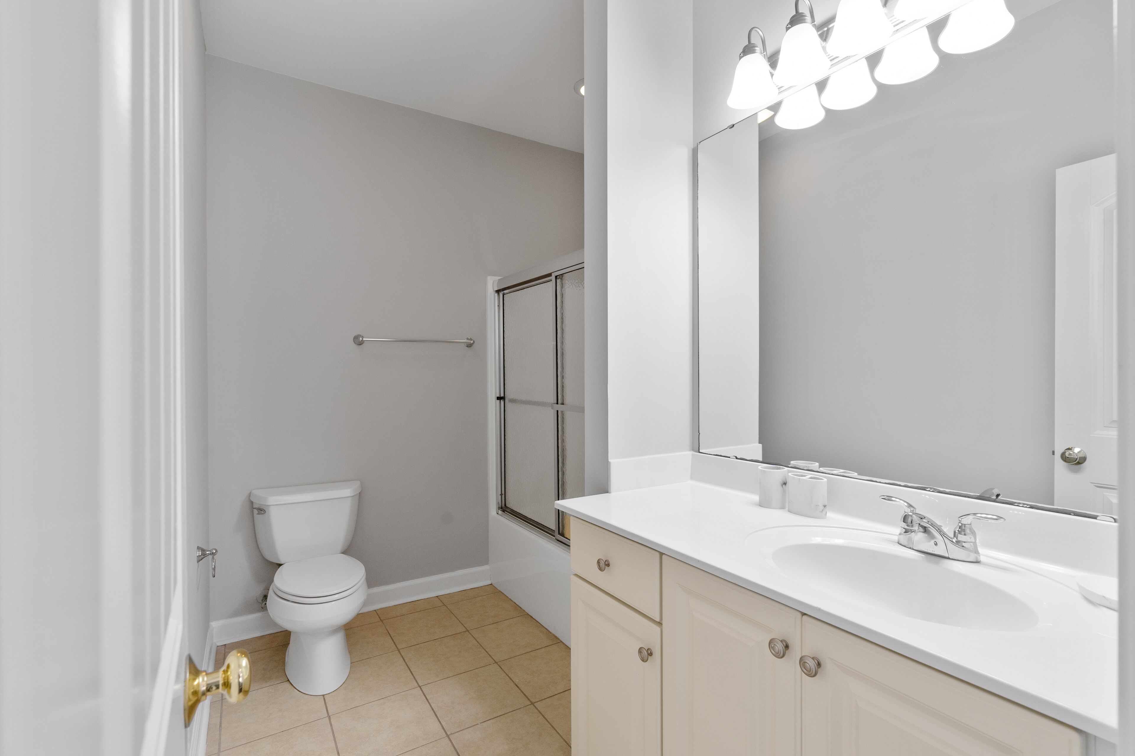 A bathroom with a toilet, shower, sink, and mirror.