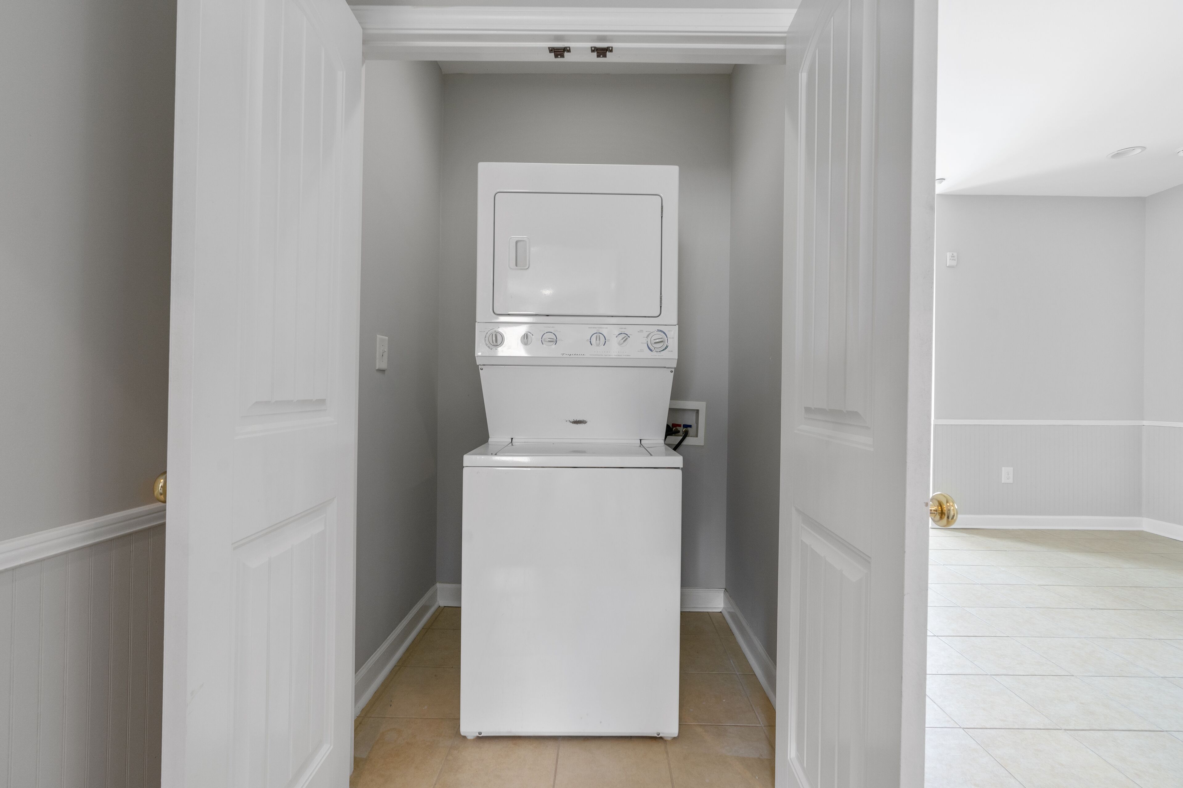 A laundry room with a front-loading washer and dryer, white walls, and a tiled floor.