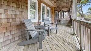 Een overdekt houten terras met Adirondack-stoelen en een houten reling.