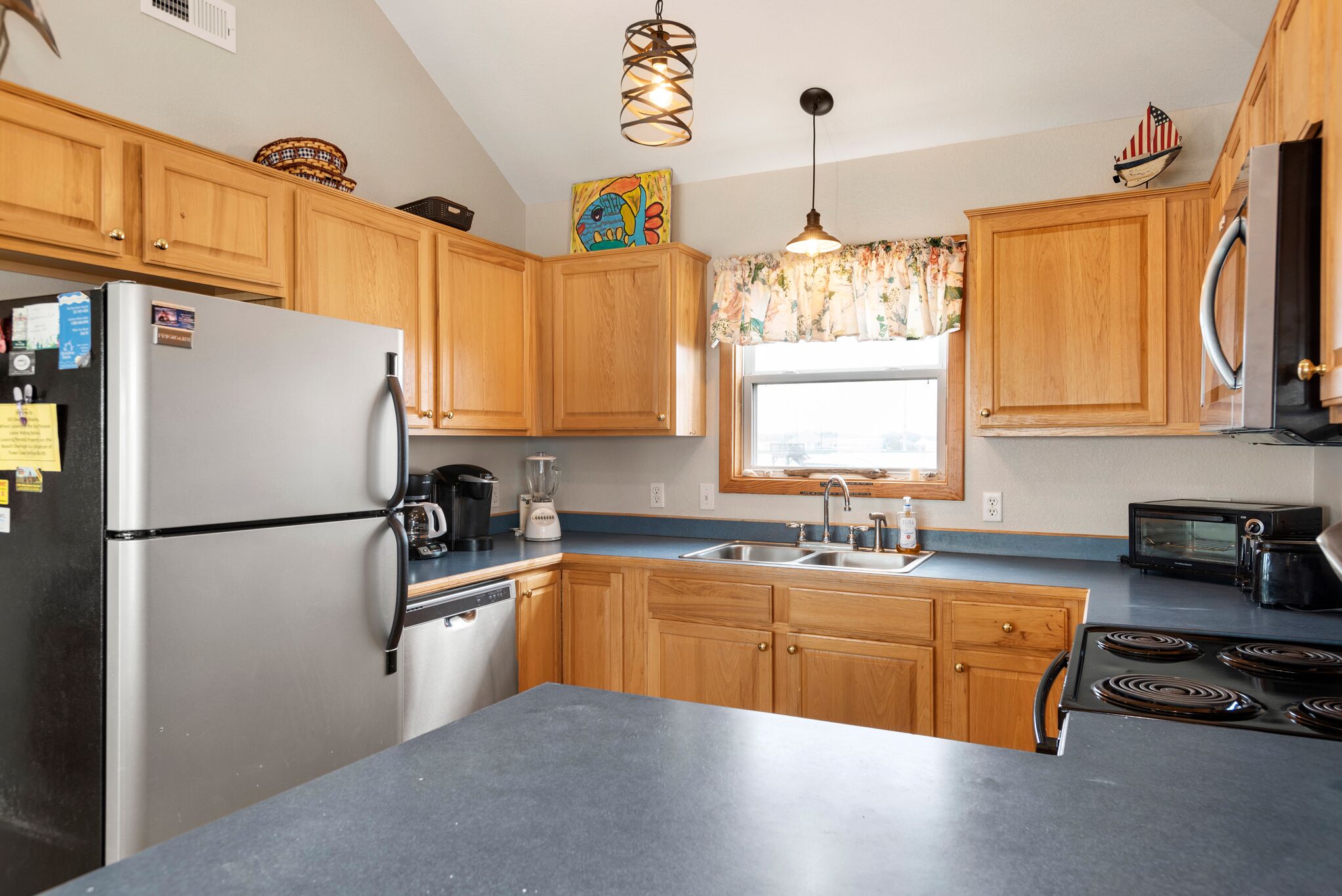 A kitchen with wooden cabinets, a stainless steel refrigerator, a stove, a sink, and a microwave.