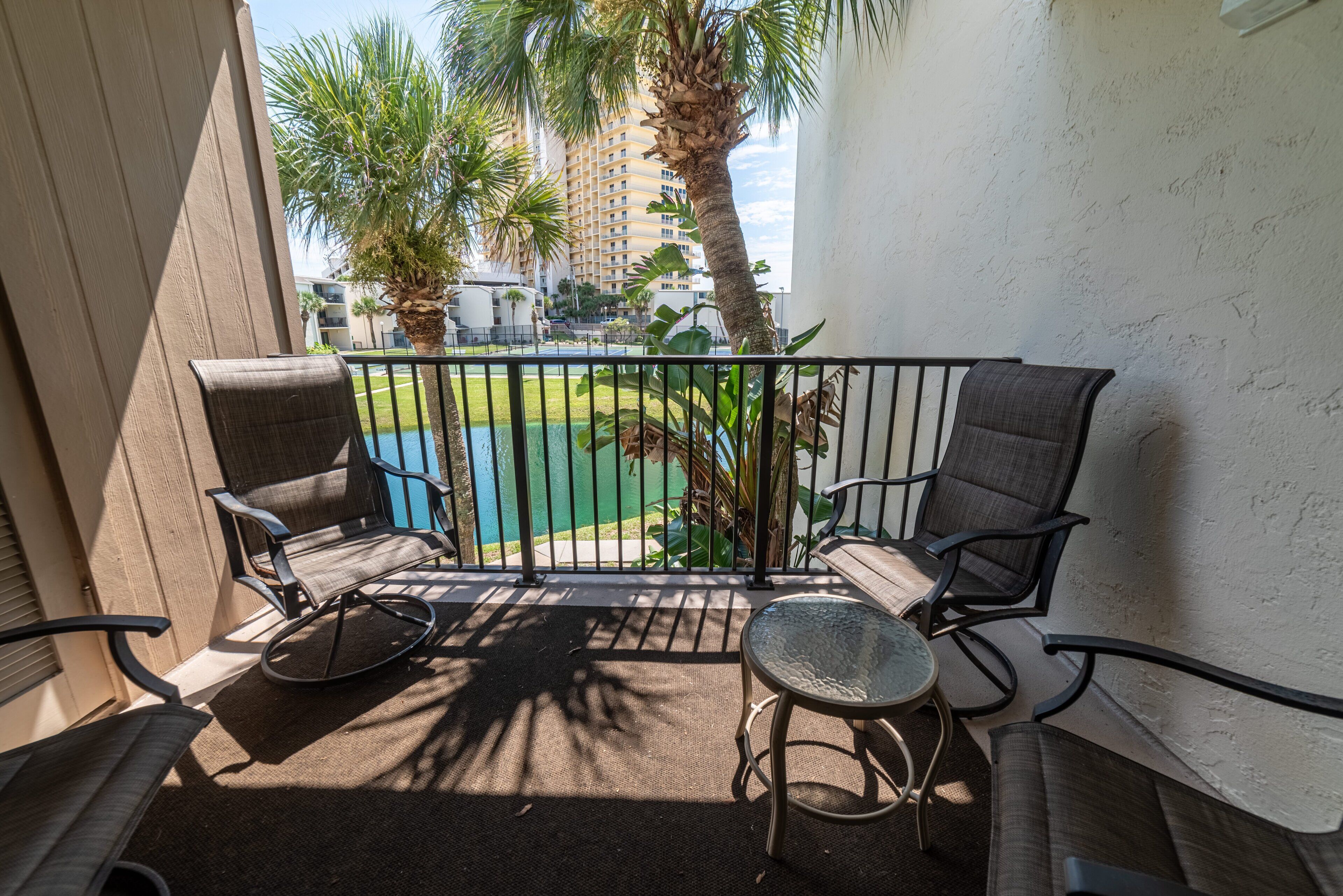 A balcony with a seating area, including a sofa and chairs, overlooking a pool and palm trees.