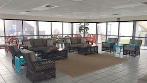 Un amplio espacio interior con mobiliario de mimbre y grandes ventanas que ofrecen vistas al exterior.