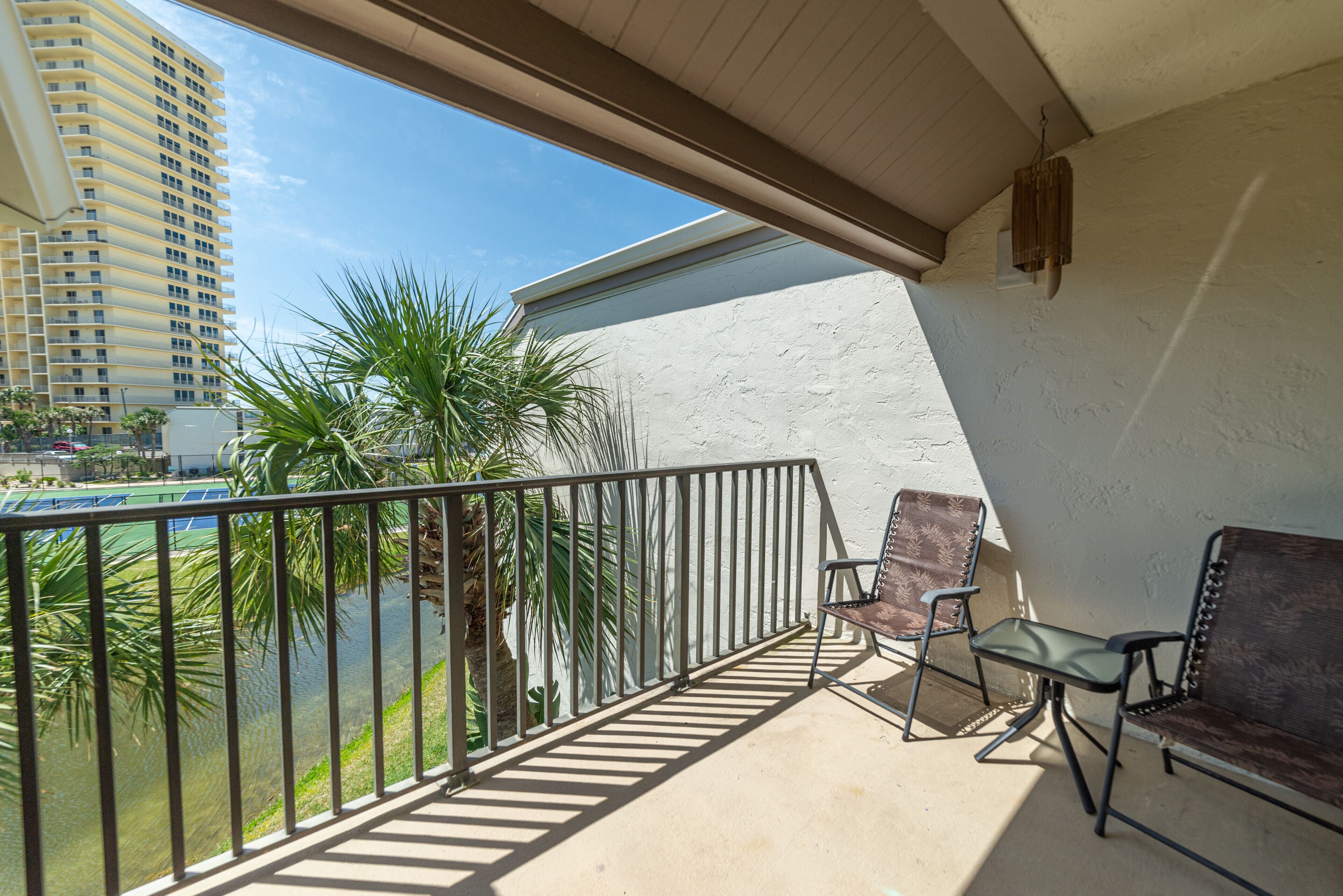 A balcony with a view of a tall building, a palm tree, and a tennis court.