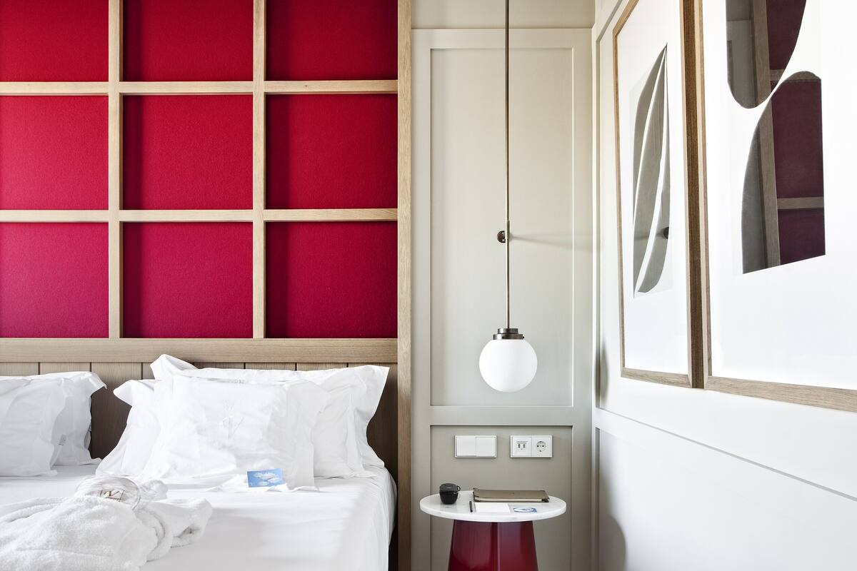 Een moderne slaapkamer, uitgevoerd in rood en wit, met een houten hoofdbord, nachtkastje met een lamp en een ingelijst schilderij aan de muur.