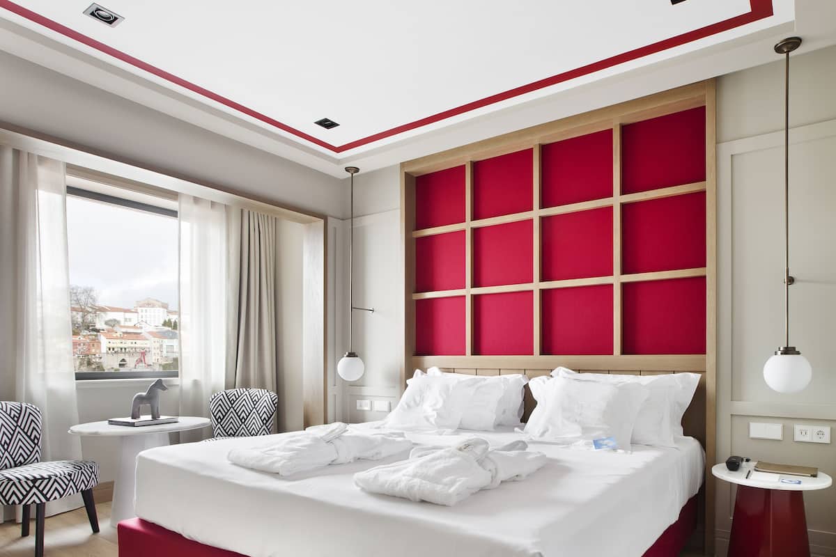 Een moderne hotelkamer met een groot bed, uitzicht op de stad, een klein rond tafeltje en een stoel.