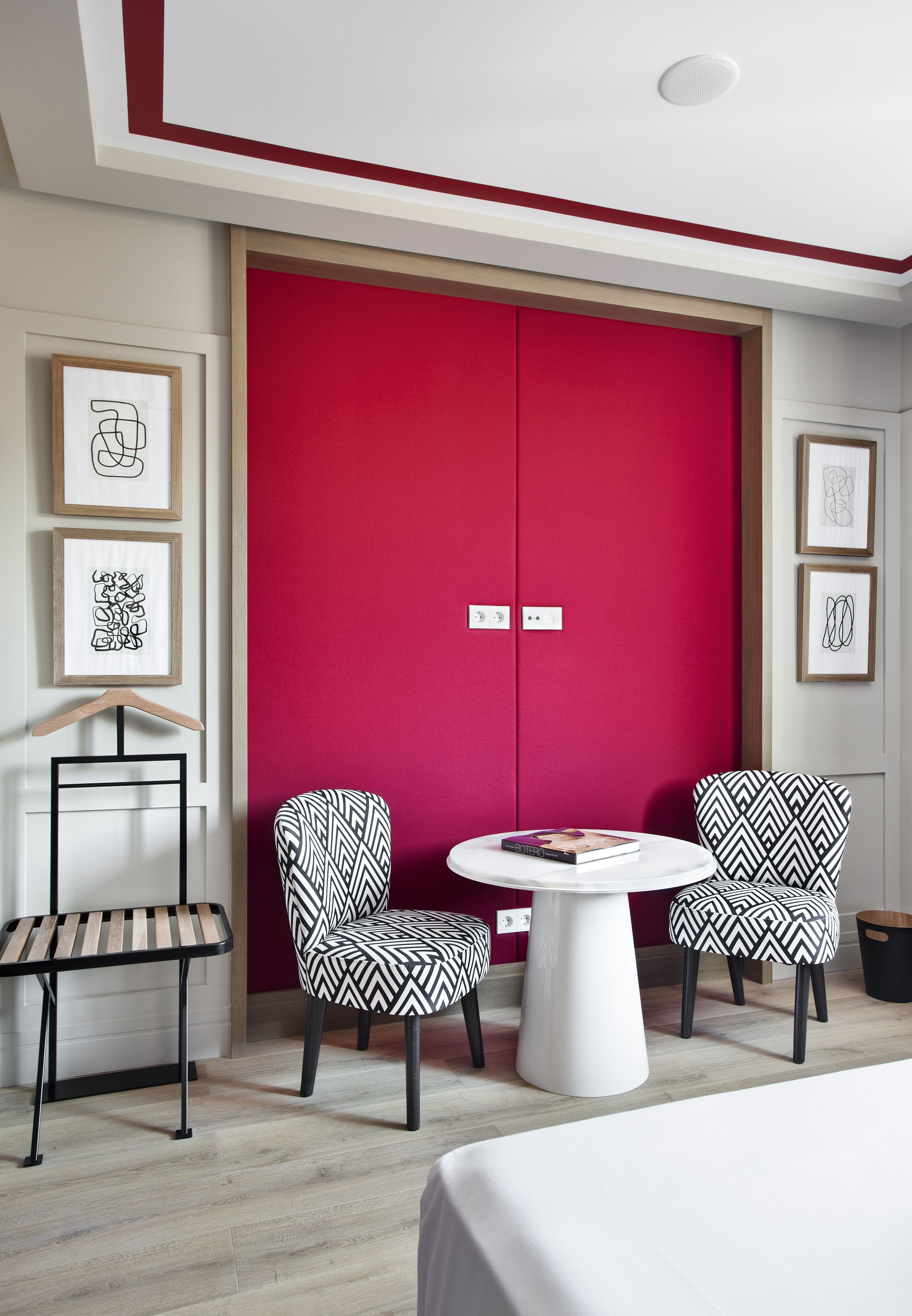 Una habitación moderna con un armario rojo, dos sillas estampadas, una mesita redonda y una silla colgante.