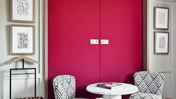 Una habitación moderna con un armario rojo, dos sillas estampadas, una mesita redonda y una silla colgante.