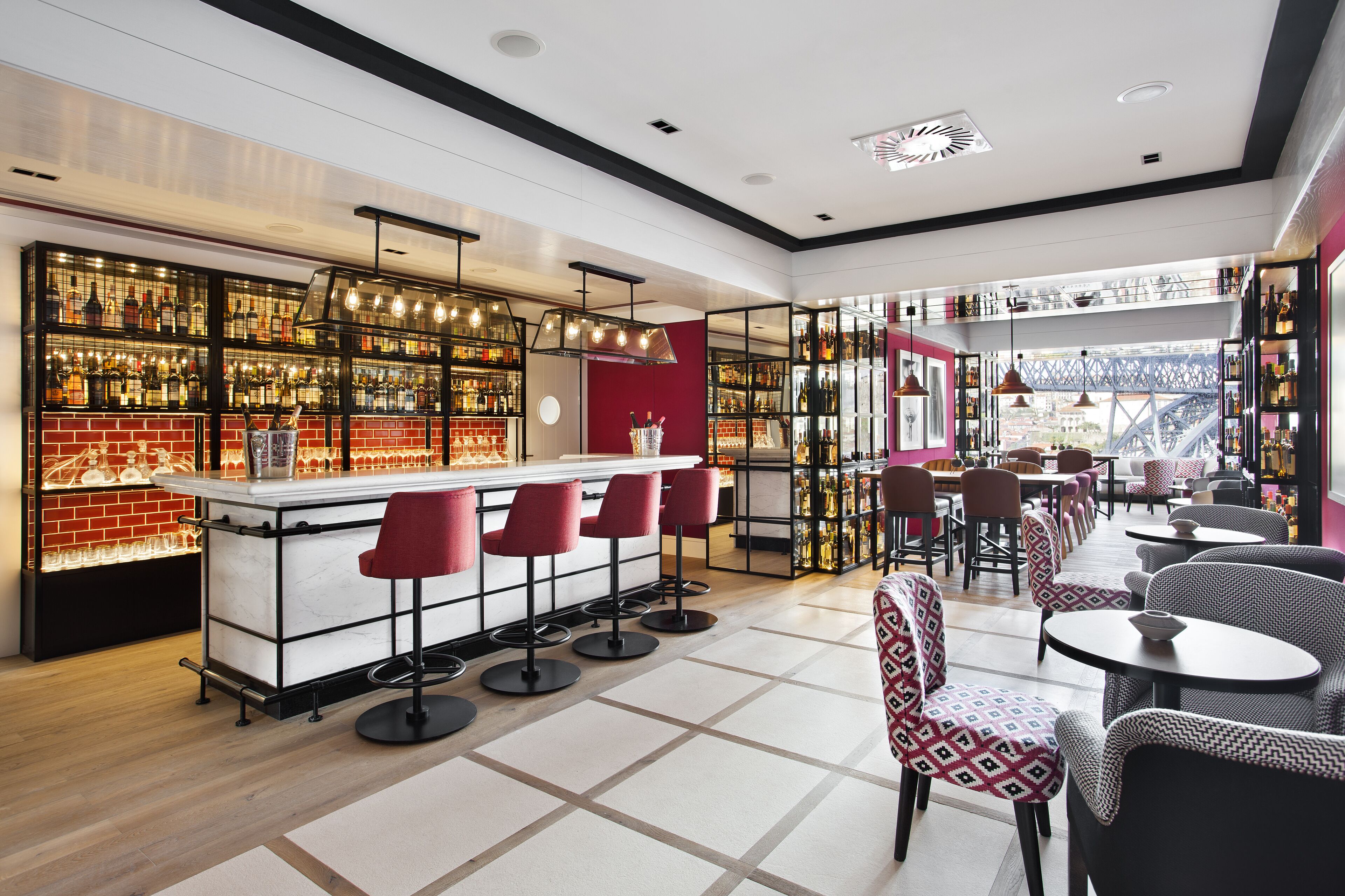 A modern bar area with a brick wall, multiple shelves of bottles, and red bar stools.