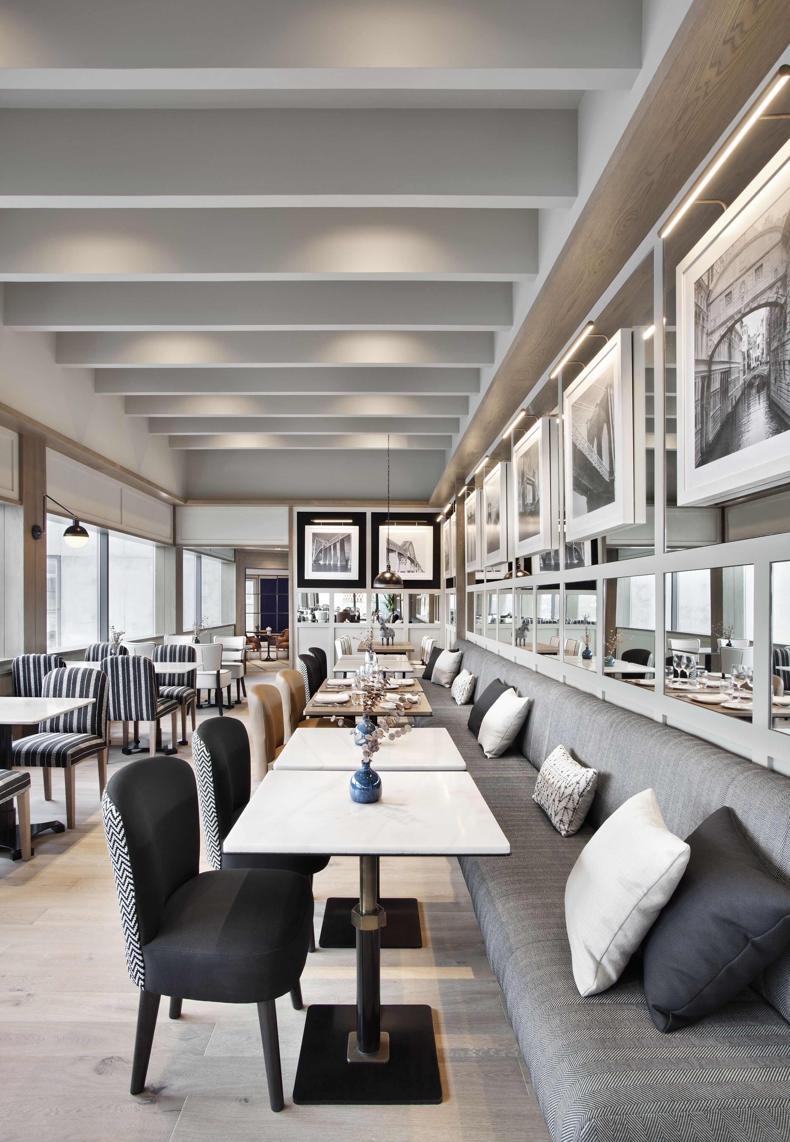 Un espace repas moderne avec une longue table, des chaises à rayures noires et blanches et un canapé gris agrémenté de coussins.