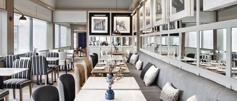 A modern dining area with a long table, black and white striped chairs, and a grey sofa with cushions.