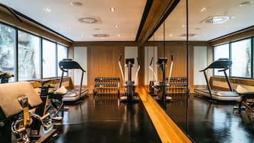 Un gimnasio con equipo de ejercicio, amplias ventanas y suelo de madera.