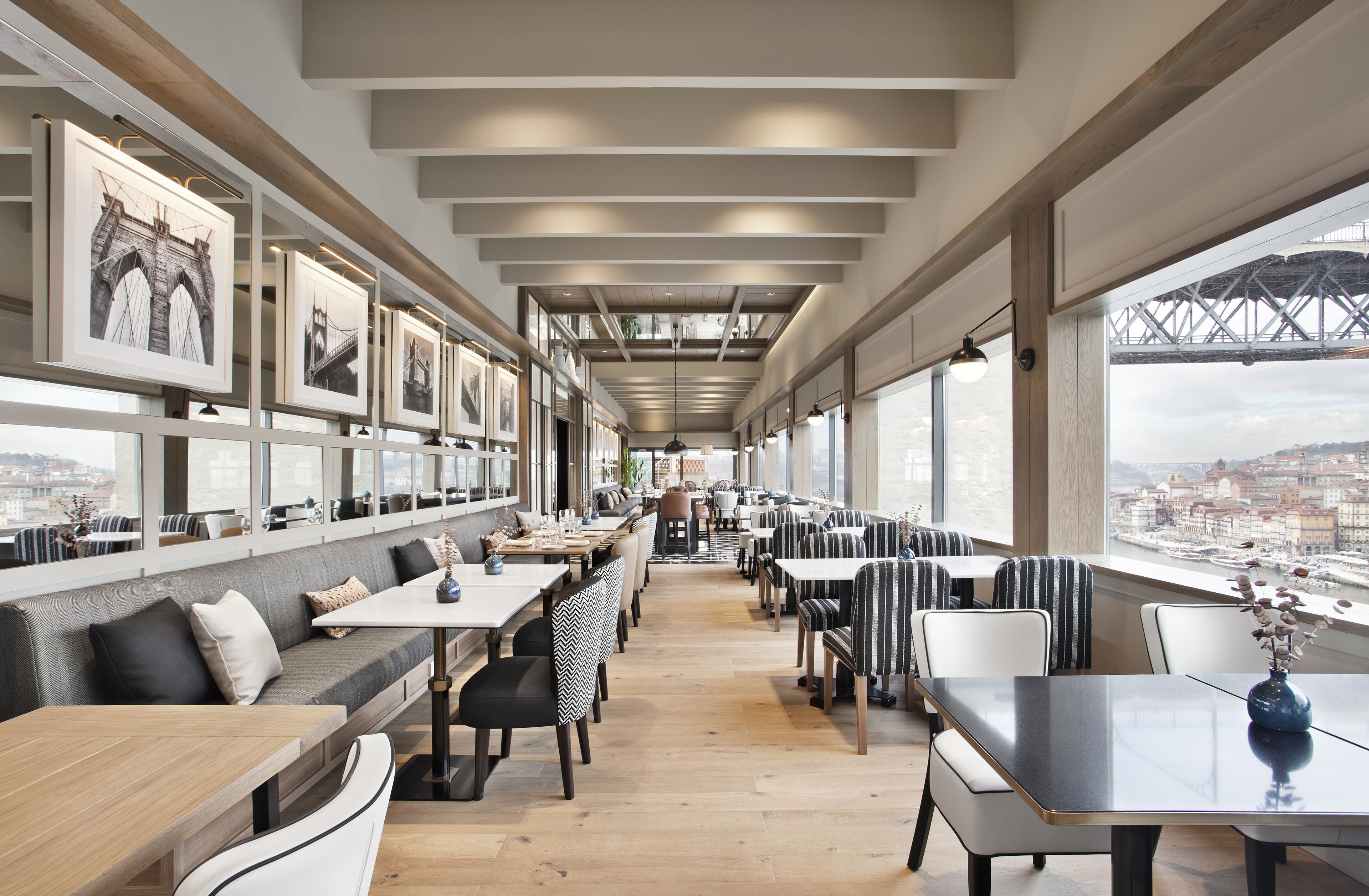 A modern restaurant with a long counter, seating area, and large windows offering a view of a bridge and cityscape.